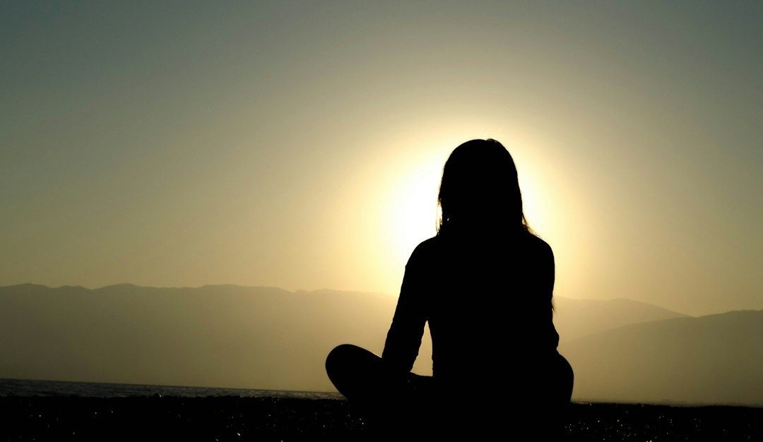 Silhouette assise en méditation face au soleil couchant